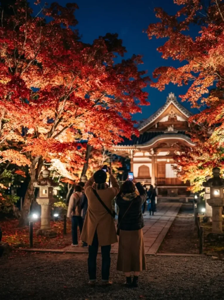 Pareja fotografiando arces iluminados de noche en un templo japonés en otoño