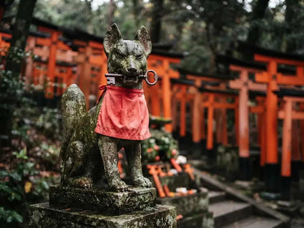 Estatua de zorro kitsune con babero rojo y llave en la boca en Fushimi Inari